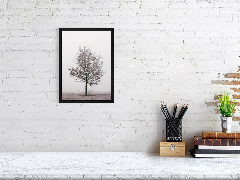 marble counter, on the right side of it a stack of several books, a container with writing implements and a small plant. On the left side, on the wall, a printed photo of a solitary oak tree in a black frame.