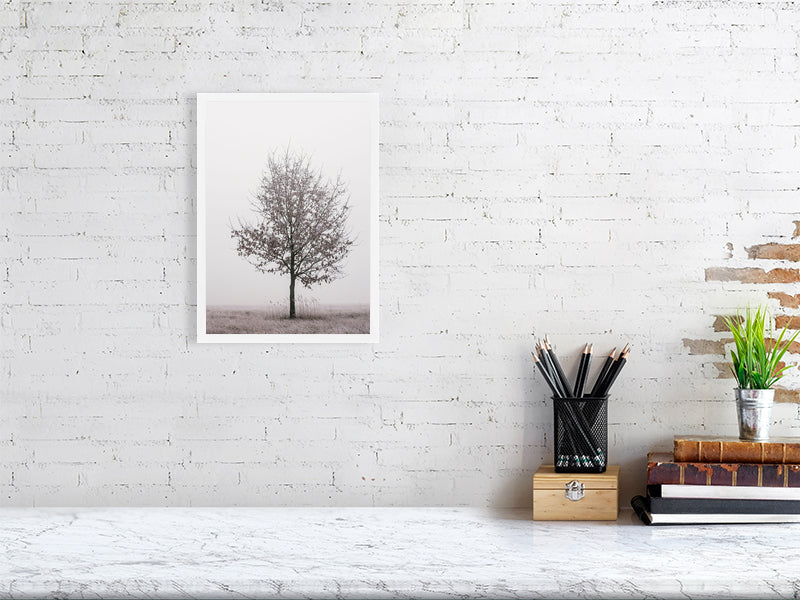 marble counter, on the right side of it a stack of several books, a container with writing implements and a small plant. On the left side, on the wall, a printed photo of a solitary oak tree in a white frame.