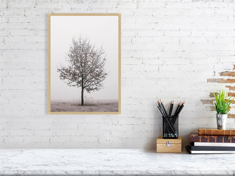 marble counter, on the right side of it a stack of several books, a container with writing implements and a small plant. On the left side, on the wall, a printed photo of a solitary oak tree in a wood frame.