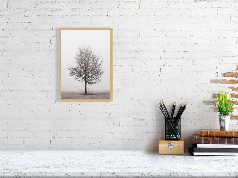 marble counter, on the right side of it a stack of several books, a container with writing implements and a small plant. On the left side, on the wall, a printed photo of a solitary oak tree in a oak frame.