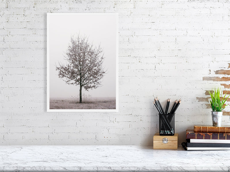 marble counter, on the right side of it a stack of several books, a container with writing implements and a small plant. On the left side, on the wall, a printed photo of a solitary oak tree in a white frame.